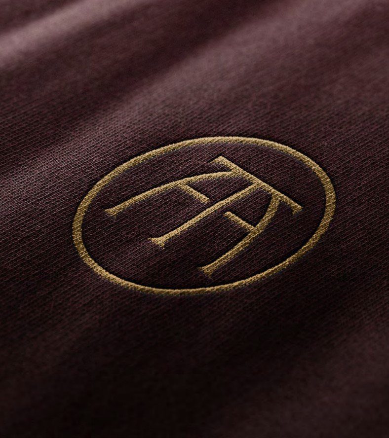Embroidered gold monogram logo on burgundy fabric, real estate brand identity